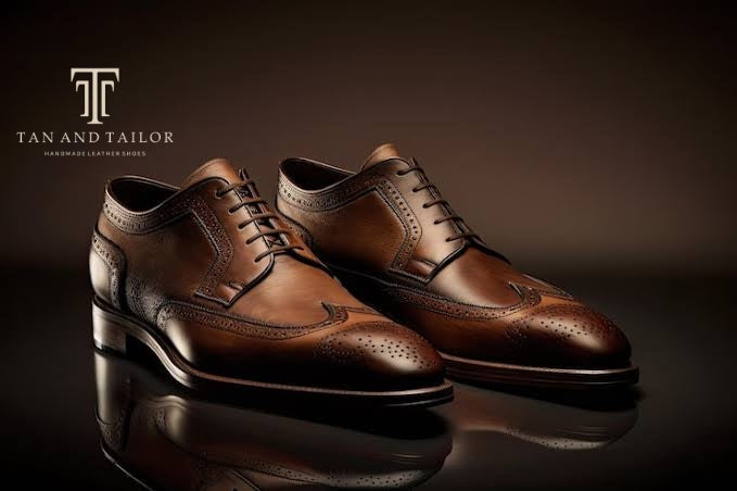 A pair of brown leather wingtip oxford shoes with brogue detailing, displayed on a dark reflective surface with a Tan and Tailor brand logo in the upper left corner.